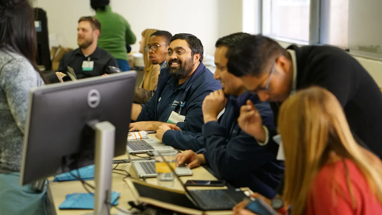 A diverse group of individuals diligently working on computers in a well-lit classroom setting.