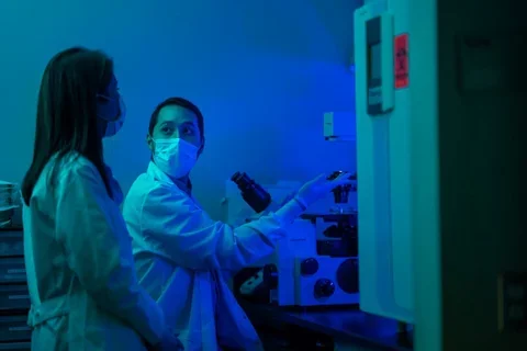 Blue light photo of Dr. Memarzradeh in lab with trainee dicussing experiments. 
