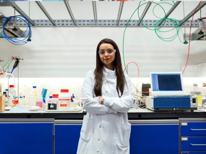 A female trainee in a lab with arms folded. 