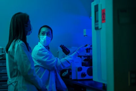 Blue light photo of Dr. Memarzradeh in lab with trainee dicussing experiments.
